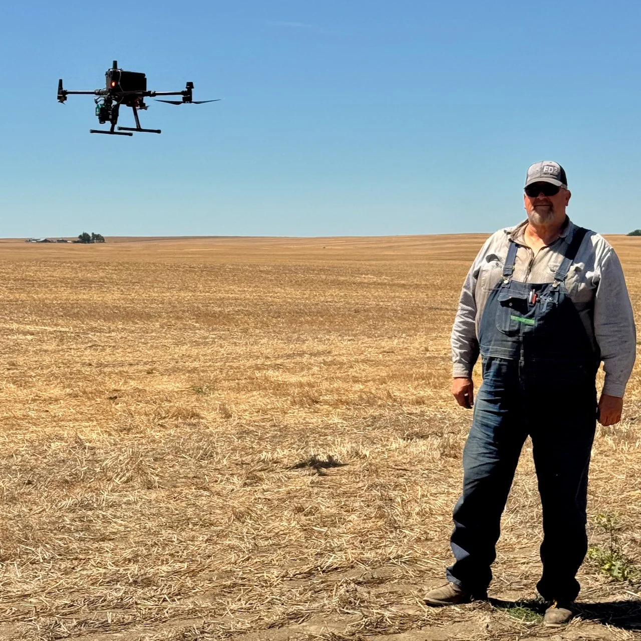 Farmer standing in a fallow field with the Agcopter drone flying overhead